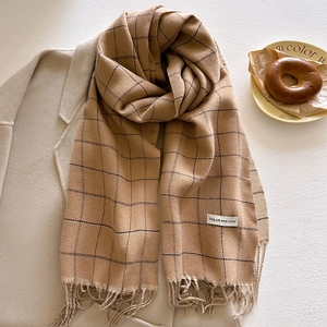 Plaid tassel scarf in camel and khaki colors draped over a stylish beige winter coat
