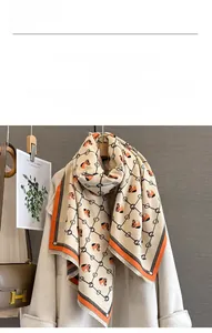 Detailed view of beige cashmere-like scarf featuring orange horse head and chain patterns
