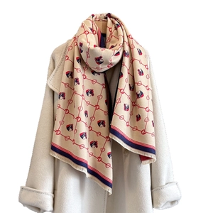 Elegant beige cashmere-feel scarf with horse pattern and red tassels on white coat