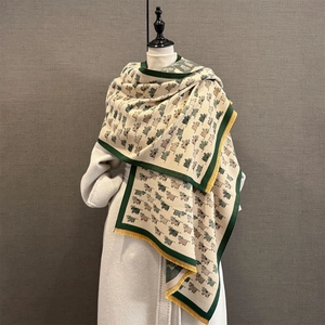 Detail of knit beige shawl featuring green cow patterns and vibrant yellow tassels