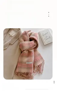Close-up of pink and beige plaid cashmere-like scarf with fringe on a white textured background