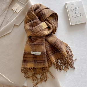Detailed view of thick cashmere-like scarf with warm brown plaid and soft fringe texture
