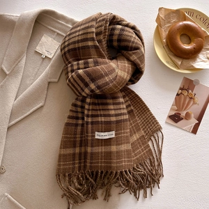 Close-up of brown plaid scarf with fringe and white brand label on a beige wool coat
