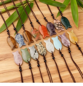 Various colorful natural stone fish pendants with woven cords on a wooden background