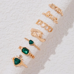 Makroaufnahme eines siebenteiligen Goldring-Sets mit smaragdgrünen Steinen und MOM-Gravur
