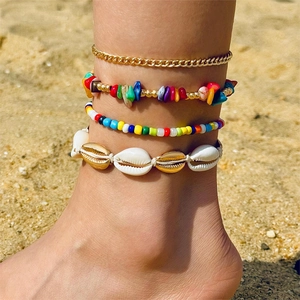 Detail of bohemian shell and multi-layer bead anklet set worn on a sunny beach