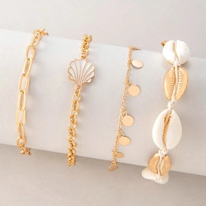 Detail of beach-style gold layered anklets with natural shells and white enamel charms