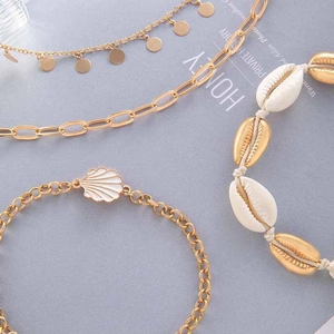 Close-up of gold shell anklet set with natural cowrie shells and enamel charms
