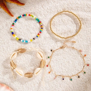 Detail of beach-style anklet set with natural shells and beads on white sand