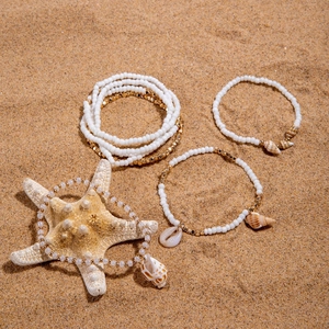 Detail shot of bohemian beaded anklet set with natural cowrie shells on sandy beach