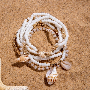 Detail of beach-style multilayer anklet set with seashells and beads on sand background
