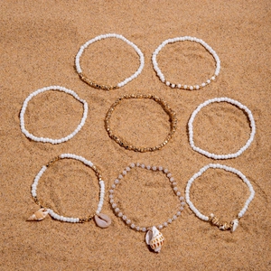 Detail of 8-piece bohemian beach jewelry set with sea shells and colorful beads on sand