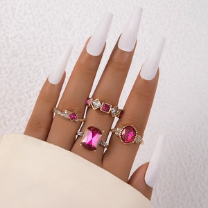 Nahaufnahme von vierteiligem Goldring-Set mit rosa Edelsteinen an Model mit weißen Nägeln