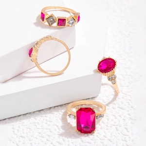 Detail eines vierteiligen Goldring-Sets mit rosaroten Edelsteinen auf weißen Steinblöcken