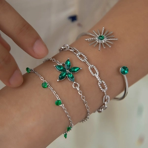 Gros plan de bracelets argentés avec pierres vertes et pendentif fleur portés au poignet