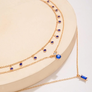 Détail macro d'un collier doré double épaisseur avec pierres bleues sur support beige
