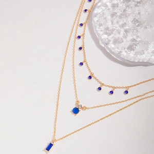 Détail d'un collier doré à trois rangs orné de pendentifs géométriques en cristal bleu
