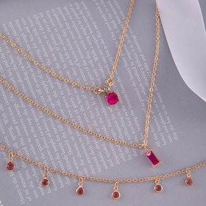 Détail macro du collier doré à trois rangs avec pendentifs en cristal rose géométrique