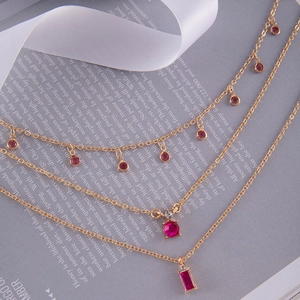 Détail d'un collier à trois couches dorées avec pendentifs en cristal rouge rubis