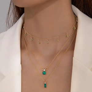 Détail d'un collier triple rang en or avec cristaux verts émeraude sur un tailleur blanc