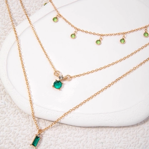 Détails de colliers superposés dorés avec des pendentifs géométriques vert émeraude