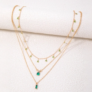Gros plan d'un collier triple rang en or avec cristaux vert émeraude sur tissu blanc
