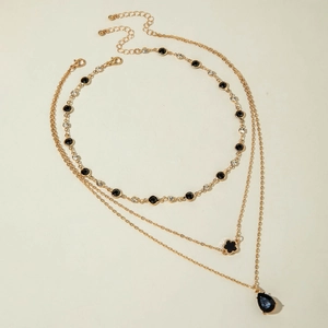 Détail d'un collier doré triple rang avec pendentifs trèfle noir et pierre en forme de goutte
