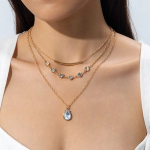 Gros plan d'un collier triple épaisseur doré avec tube et pendentif goutte sur mannequin