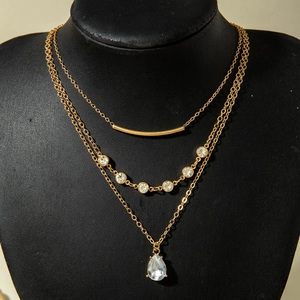 Détail d'un collier doré triple couche avec zircons et pendentif en forme de goutte