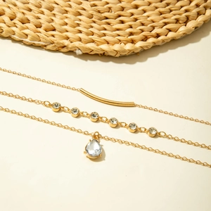 Détail d'un collier multicouche doré avec tube poli et pendentif goutte de cristal