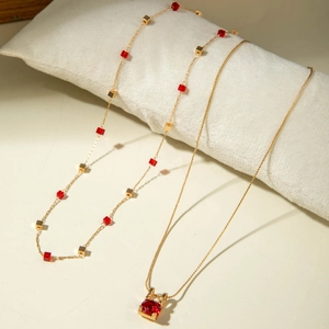 Détail d'un collier triple rang en or avec gemmes rouges sur un coussin de présentation