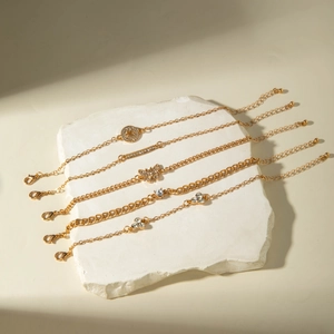 Detailed close-up of 5-piece gold bracelet set with butterfly and heart charms on stone tray