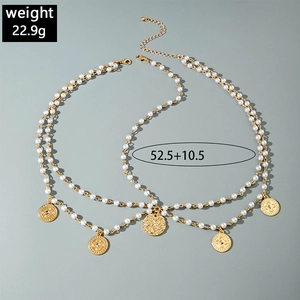 Bohemian gold pearl layered necklace with engraved coin pendants on gray background
