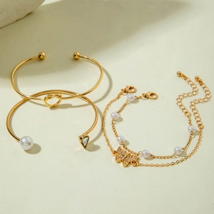 Close-up of gold-toned bracelet set with pearls, knotted cuff, and butterfly charm detail