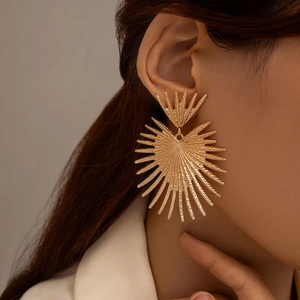 Close-up of oversized gold geometric sunburst earrings worn by a model in soft lighting