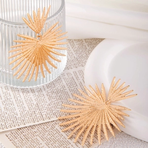 Macro shot of gold sunburst earrings with hammered texture on white ceramic plate