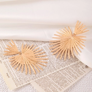 Macro detail of sunburst textured earrings in warm gold finish on a vintage paper background