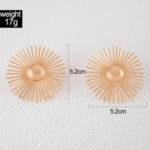 Detail of gold sunflower earrings showing a 5.2cm diameter and 17g weight on white surface