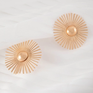 Macro shot of gold sunburst flower earrings on soft white silk background texture