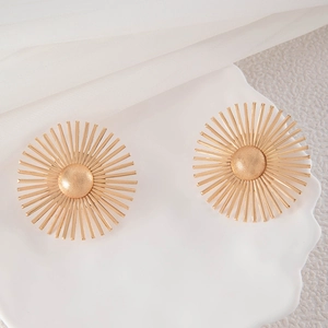 Detail shot of golden sunburst drop earrings with matte center on white textured backdrop