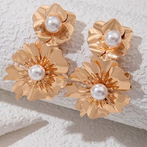 Detail of gold floral petal earrings with white pearls on a textured white stand