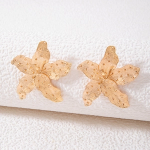 Macro detail of gold starfish earrings with brushed metal texture on white props