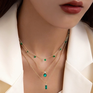 Collier doré à trois rangs avec pendentifs géométriques verts sur un costume blanc chic