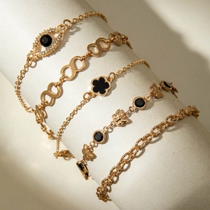 Détail d'un ensemble de 5 bracelets dorés avec trèfle noir, œil protecteur et papillons