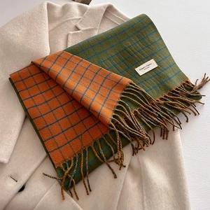 Close-up of double-sided plaid scarf with emerald green and orange tones with long tassels