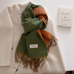 Detail of green and orange plaid scarf with woven tassel fringe and white logo tag