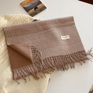 Detail of classic brown plaid scarf featuring soft fringe and elegant label on knit fabric