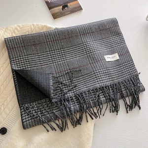 Classic black and gray plaid scarf with elegant tassels and woven label on a sweater