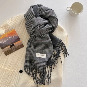 Detail of soft plaid scarf with fringe on a white knit sweater with a coffee mug