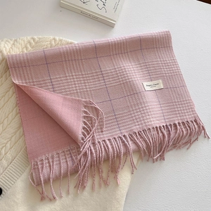Thick pink plaid scarf with tassels laid on white knit sweater and decorative book